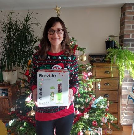 Winner of food waste blender holds her prize and stands in front of a Christmas tree