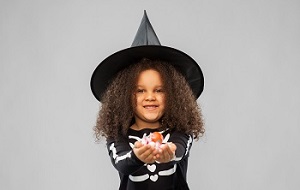 Girl in a witch's hat holding sweets in her hands